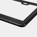 Close-up of Karbon Technik black woven carbon fibre car licence plate frame, showing weave detail and a mounting hole.