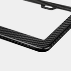 Close-up of Karbon Technik black woven carbon fibre car licence plate frame, showing weave detail and a mounting hole.