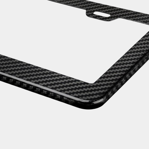 Close-up of Karbon Technik black woven carbon fibre car licence plate frame, showing weave detail and a mounting hole.